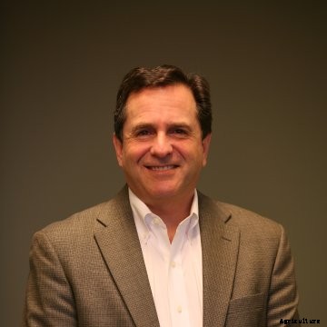 Rich Ansell of Mahindra poses for a portrait wearing a brown suit and white collared shirt