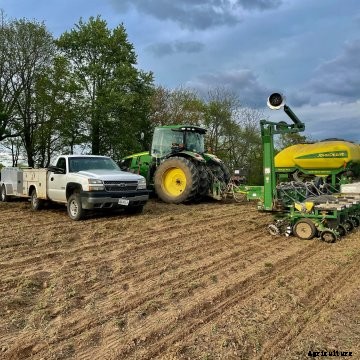 A white Chevy truck and trailer with a green John Deere tractor and planter in the field