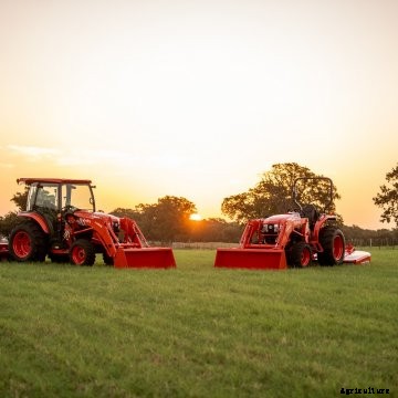 Two new models of Kubota compact tractors sit in a pasture at sunrise