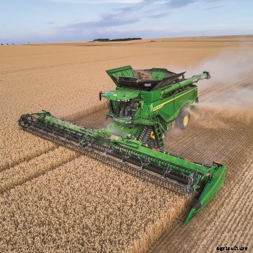a green John Deere X9 combine harvests a field of wheat in Europe
