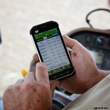 Farmer holding a smartphone in the cab of a tractor