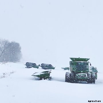 Snow on John Deere combine and headers sitting on the edge of a farm field