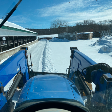 A blue tractor pushes snow
