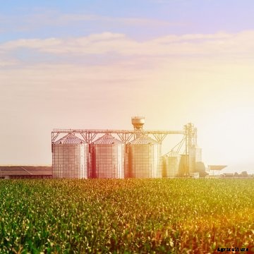 The sun sets behind grain bins on a farm.