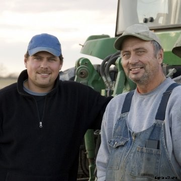 Two smiling farmers stand next to a tractor.