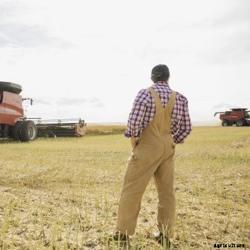 A farmer standing in his field with a combine in the background.