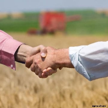 Two farmers shaking hands with a wheat field in the background.