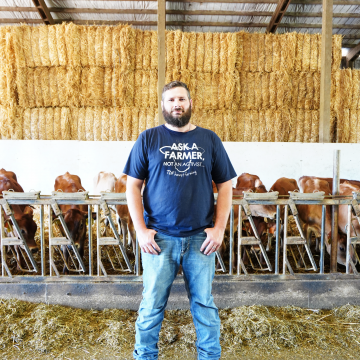 Oregon dairy farmer and author Derrick Josi stands in his cattle barn wearing a blue shirt and jeans
